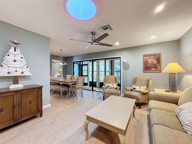 living room with ceiling fan, light hardwood / wood-style floors, and a textured ceiling