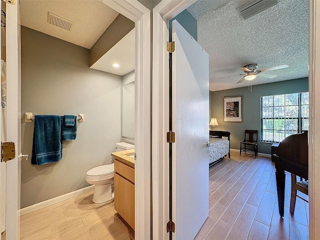 bathroom with vanity, a textured ceiling, ceiling fan, wood-type flooring, and toilet