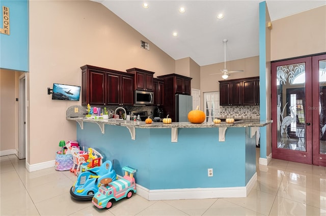 kitchen featuring kitchen peninsula, a kitchen bar, stainless steel appliances, ceiling fan, and high vaulted ceiling