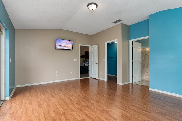 unfurnished bedroom with a textured ceiling, light wood-type flooring, a spacious closet, and vaulted ceiling