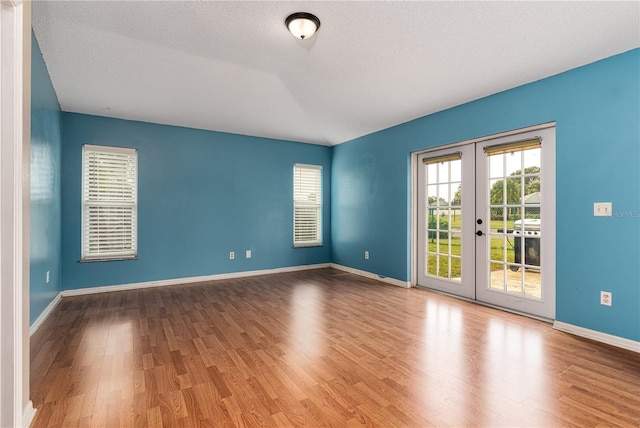 spare room with hardwood / wood-style floors, a textured ceiling, vaulted ceiling, and french doors