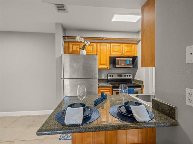 kitchen with dark stone counters, stainless steel appliances, brown cabinets, baseboards, and visible vents