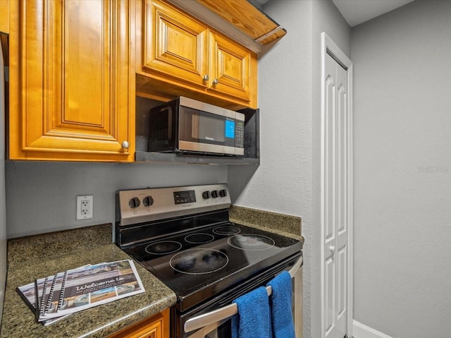 kitchen with dark countertops, brown cabinetry, stainless steel appliances, and baseboards