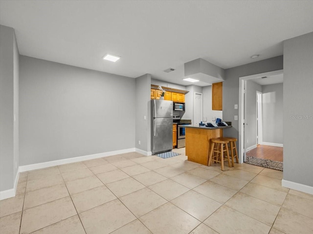 kitchen with light tile patterned floors, appliances with stainless steel finishes, baseboards, a peninsula, and a kitchen breakfast bar