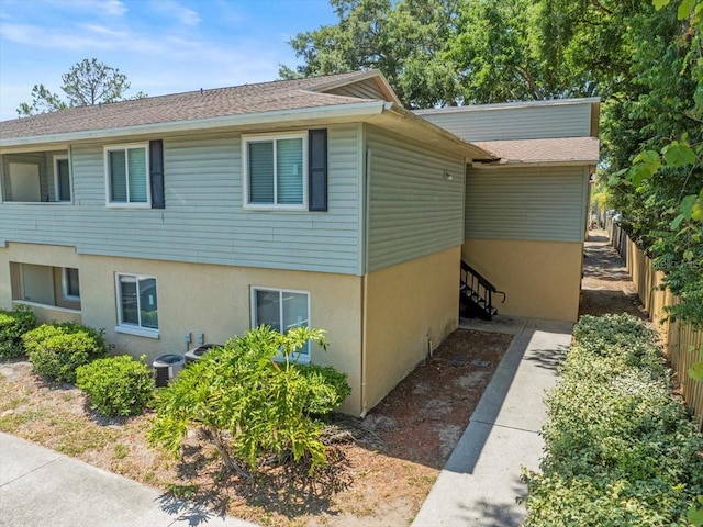 view of property exterior featuring fence, stucco siding, central AC unit, and roof with shingles