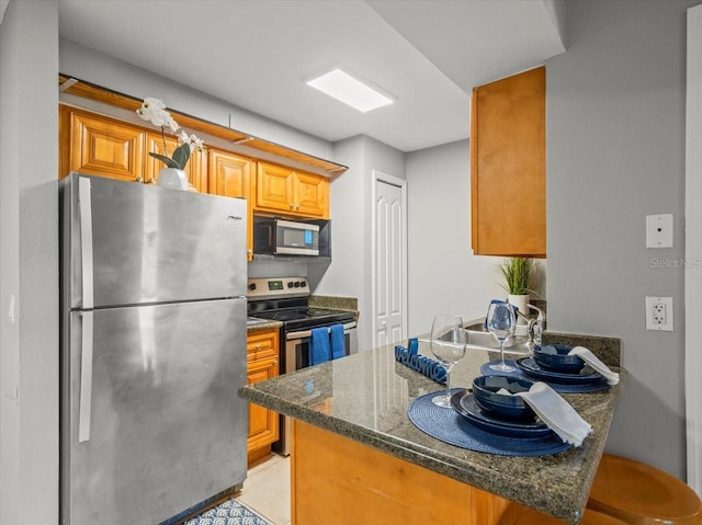 kitchen with brown cabinetry, stainless steel appliances, a peninsula, and dark stone counters