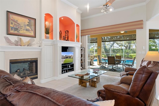 living room featuring ceiling fan, light tile patterned floors, ornamental molding, and a towering ceiling