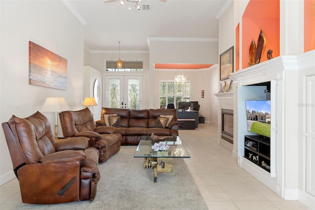 tiled living room with ceiling fan with notable chandelier, ornamental molding, a high ceiling, and french doors