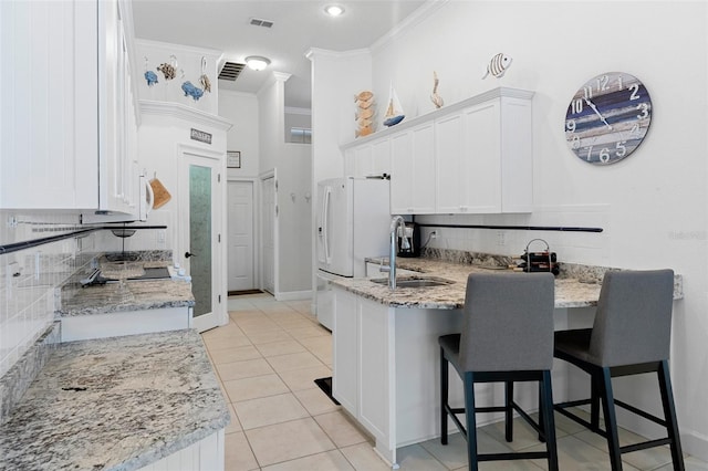 kitchen featuring white refrigerator with ice dispenser, white cabinetry, crown molding, and light stone counters