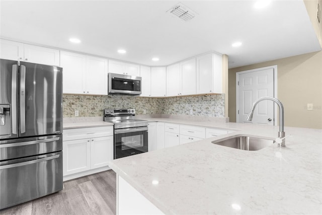 kitchen featuring appliances with stainless steel finishes, light wood-type flooring, light stone counters, sink, and white cabinetry