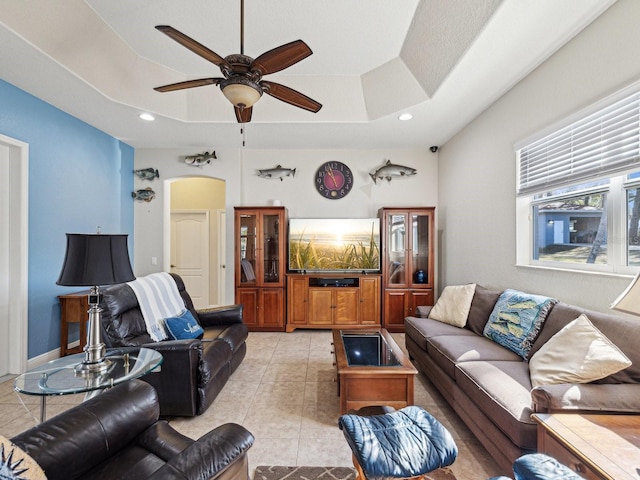 living room with light tile patterned floors, a raised ceiling, and ceiling fan