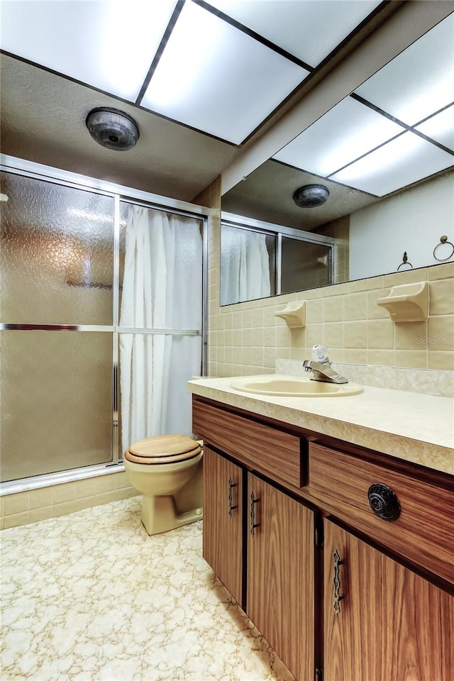 bathroom featuring an enclosed shower, vanity, toilet, and backsplash