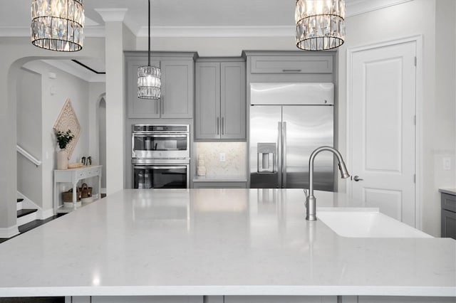 kitchen with gray cabinetry, stainless steel appliances, light stone counters, a large island with sink, and decorative light fixtures