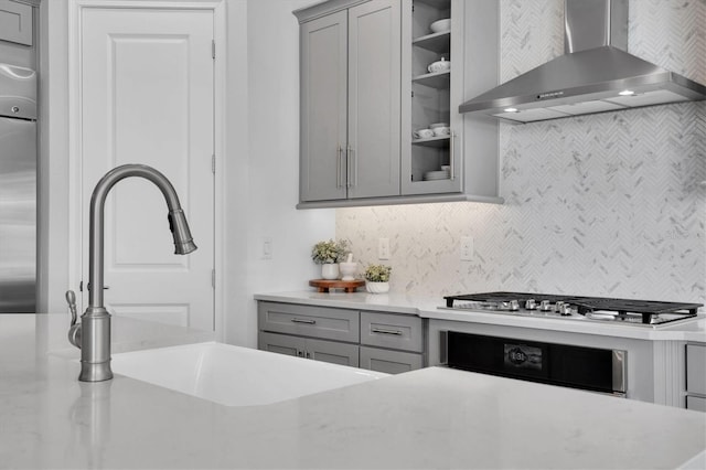 kitchen featuring gray cabinetry, sink, wall chimney exhaust hood, appliances with stainless steel finishes, and tasteful backsplash