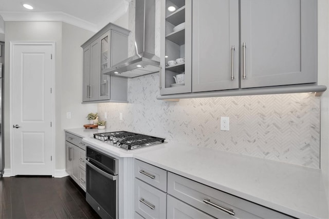 kitchen featuring stainless steel appliances, wall chimney range hood, backsplash, crown molding, and gray cabinets