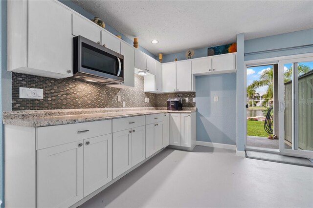 kitchen featuring white cabinets, a textured ceiling, light stone counters, and backsplash