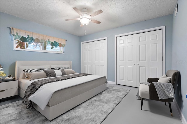 bedroom with concrete flooring, a textured ceiling, ceiling fan, and multiple closets