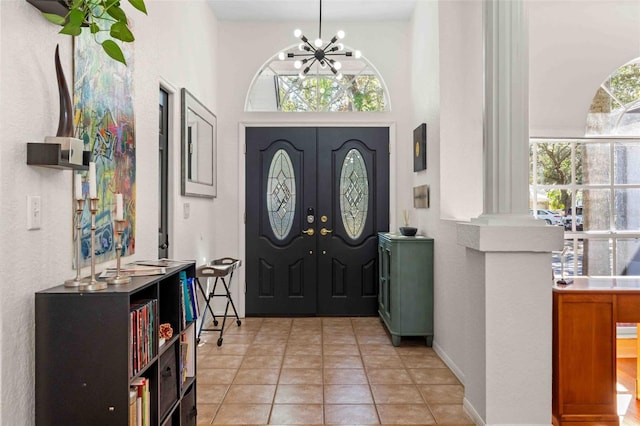 entrance foyer featuring decorative columns, light tile patterned floors, and an inviting chandelier