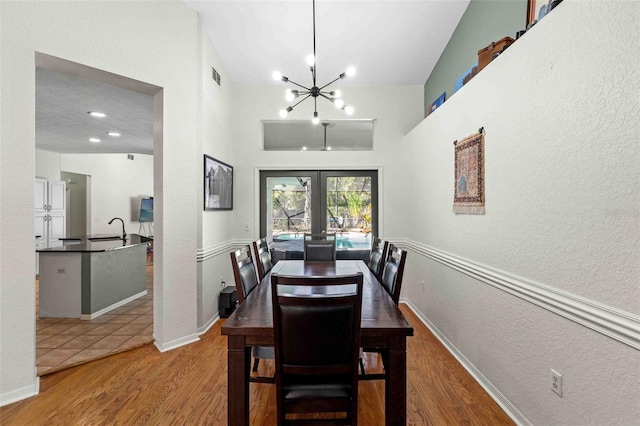 dining area with french doors, sink, wood-type flooring, a notable chandelier, and lofted ceiling