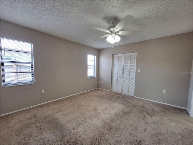 unfurnished bedroom featuring ceiling fan, light colored carpet, a textured ceiling, and a closet