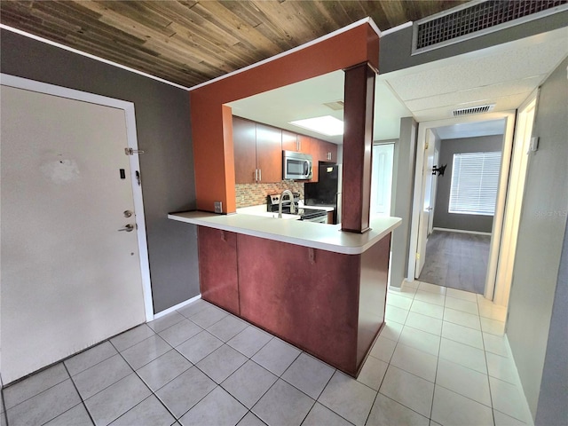 kitchen featuring backsplash, kitchen peninsula, light tile patterned floors, and appliances with stainless steel finishes