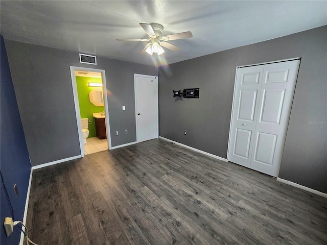 unfurnished bedroom featuring dark hardwood / wood-style floors, ceiling fan, ensuite bathroom, and a closet