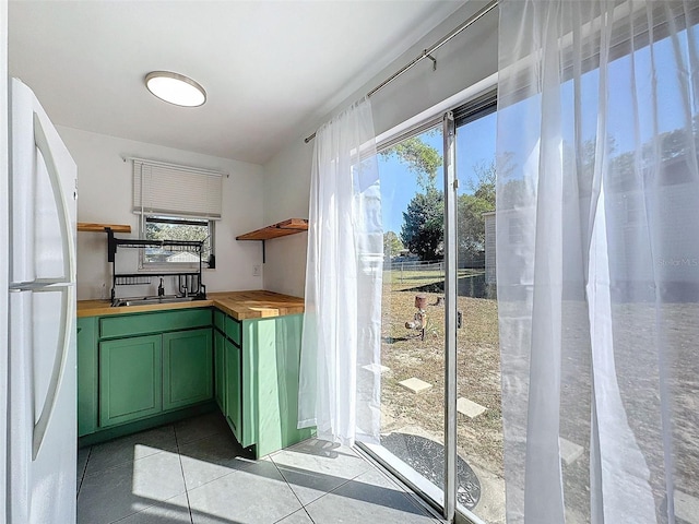 kitchen featuring sink, light tile patterned floors, white refrigerator, butcher block countertops, and green cabinets