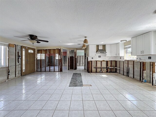 kitchen featuring white cabinets, wall chimney exhaust hood, ceiling fan, light tile patterned floors, and a textured ceiling