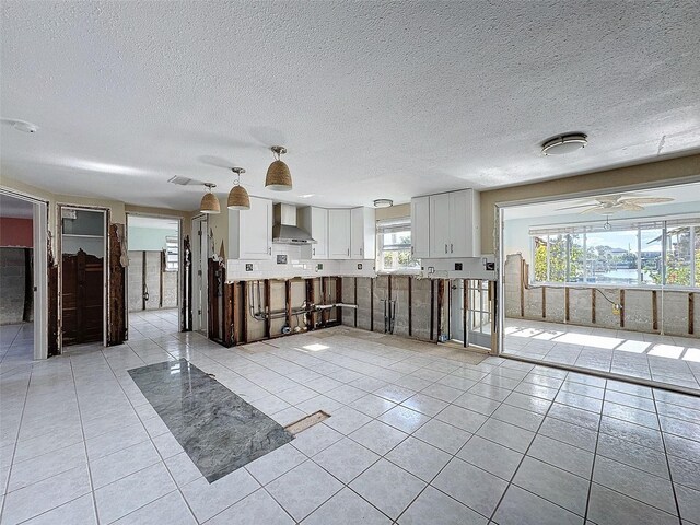 kitchen featuring light tile patterned flooring, white cabinetry, a textured ceiling, and wall chimney range hood