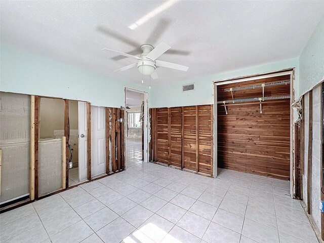 unfurnished bedroom featuring ceiling fan, wooden walls, light tile patterned floors, and a textured ceiling