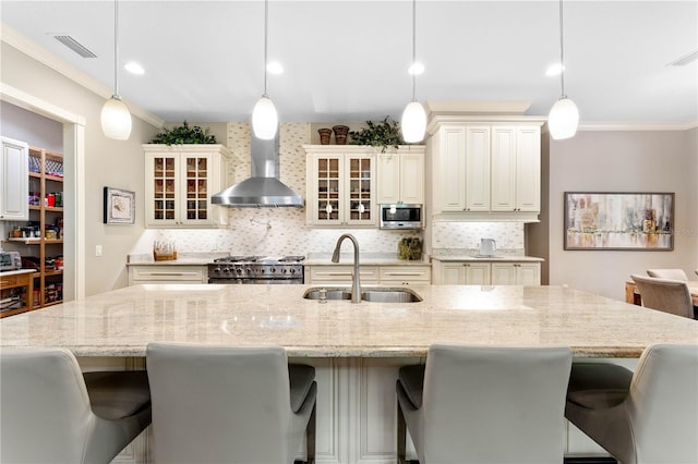 kitchen featuring a kitchen breakfast bar, sink, wall chimney exhaust hood, appliances with stainless steel finishes, and decorative light fixtures