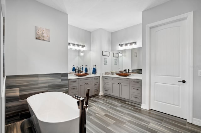 bathroom with hardwood / wood-style flooring, vanity, a tub to relax in, and tile walls