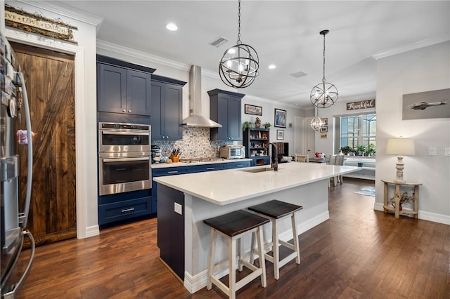 kitchen with wall chimney range hood, sink, an island with sink, a kitchen bar, and stainless steel appliances