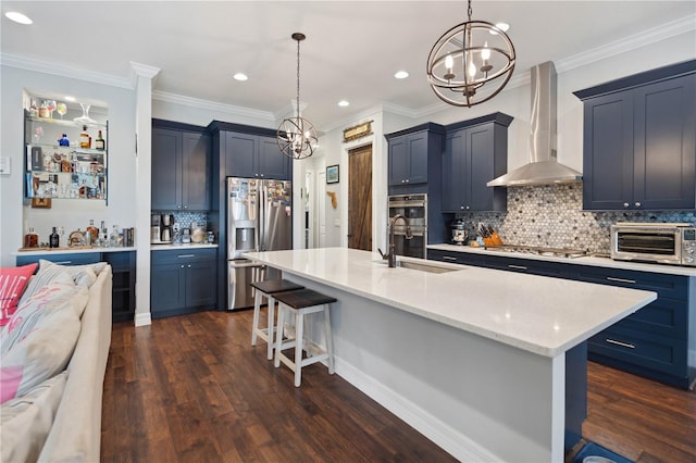 kitchen with appliances with stainless steel finishes, hanging light fixtures, wall chimney exhaust hood, and sink