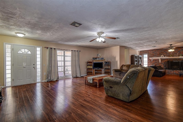 living room with a textured ceiling, dark hardwood / wood-style floors, ceiling fan, and a fireplace