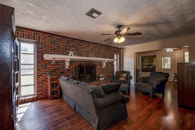 living room with dark hardwood / wood-style flooring, brick wall, a textured ceiling, ceiling fan, and a fireplace