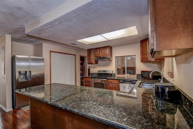 kitchen with kitchen peninsula, dark stone countertops, stainless steel appliances, and dark hardwood / wood-style floors