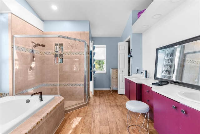 bathroom with wood finished floors, double vanity, a sink, a shower stall, and a bath