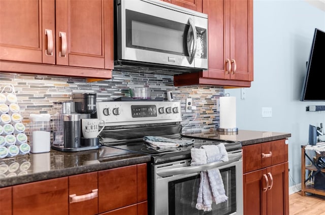 kitchen with decorative backsplash, dark stone countertops, appliances with stainless steel finishes, and light wood-style floors