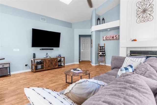 living room with visible vents, high vaulted ceiling, a tiled fireplace, wood finished floors, and baseboards