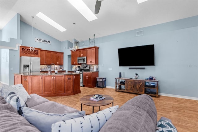 living room with baseboards, visible vents, high vaulted ceiling, a skylight, and light wood-style floors