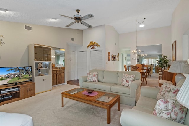 living room with ceiling fan with notable chandelier, light colored carpet, a textured ceiling, and high vaulted ceiling