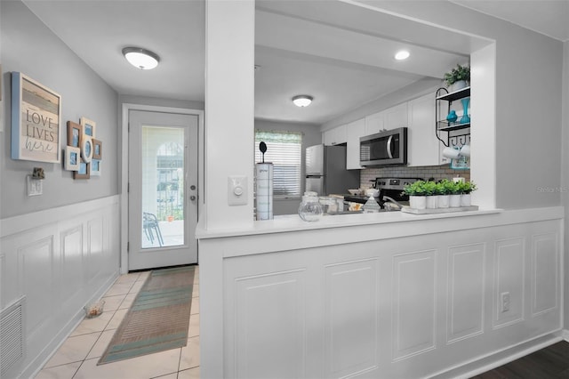 kitchen featuring kitchen peninsula, light tile patterned floors, appliances with stainless steel finishes, tasteful backsplash, and white cabinetry