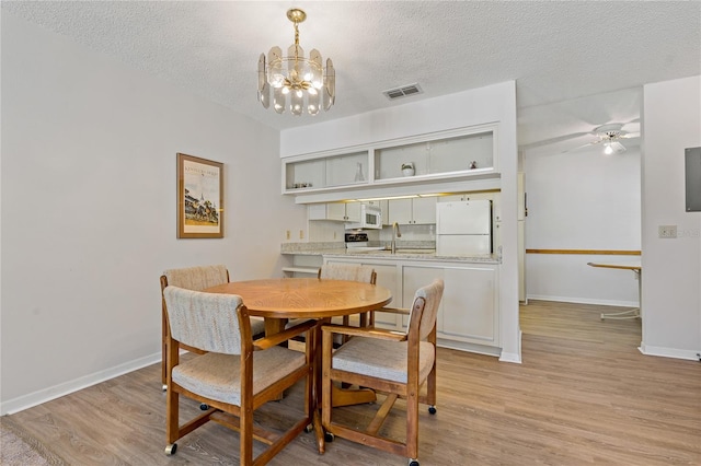 dining area featuring sink, ceiling fan with notable chandelier, a textured ceiling, and light wood-type flooring