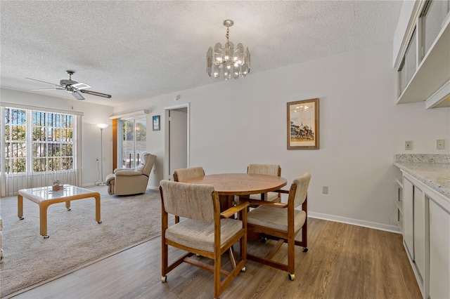 dining space with ceiling fan with notable chandelier, a textured ceiling, and light wood-type flooring