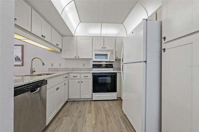 kitchen with sink, light stone counters, light hardwood / wood-style floors, white appliances, and white cabinets