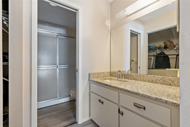 bathroom with hardwood / wood-style floors, vanity, toilet, and a shower with door