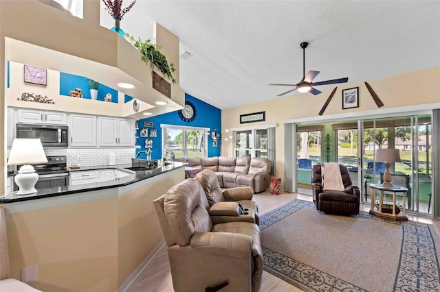 living room featuring high vaulted ceiling, sink, light hardwood / wood-style flooring, ceiling fan, and a textured ceiling