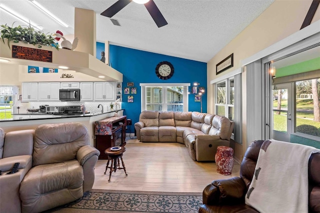 living room featuring ceiling fan, sink, light hardwood / wood-style flooring, high vaulted ceiling, and a textured ceiling