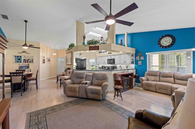 living room featuring a textured ceiling, light hardwood / wood-style floors, high vaulted ceiling, and ceiling fan